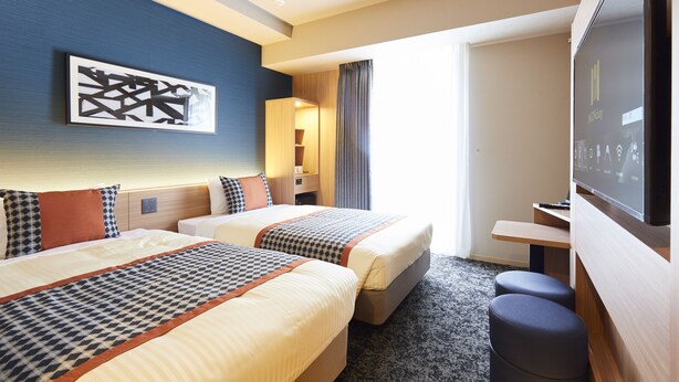 A hotel room with two beds, a TV, a desk, and a painting on the wall.