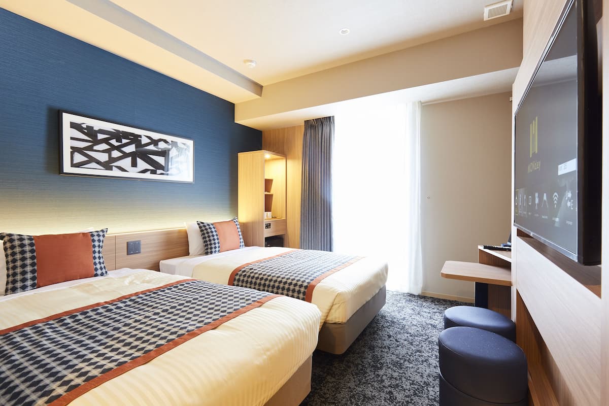 A hotel room with two beds, a TV, a desk, and a painting on the wall.