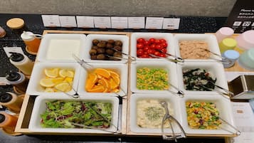 A buffet with various food options including salads, fruits, and meat dishes.