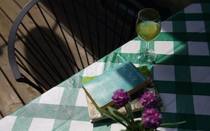 Una mesa con mantel a cuadros, un libro titulado 'Pretty One Day', un vaso de bebida y una silla.