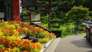 A wooden pathway leading through a garden with vibrant flower beds and neatly trimmed bushes. - Byeolmuri Pension (Hoengseong)
