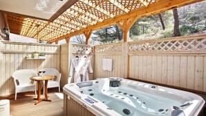 A wooden deck with a hot tub, wicker chairs, and a small table with a book and wine glasses. - Byeolmuri Pension (Hoengseong)