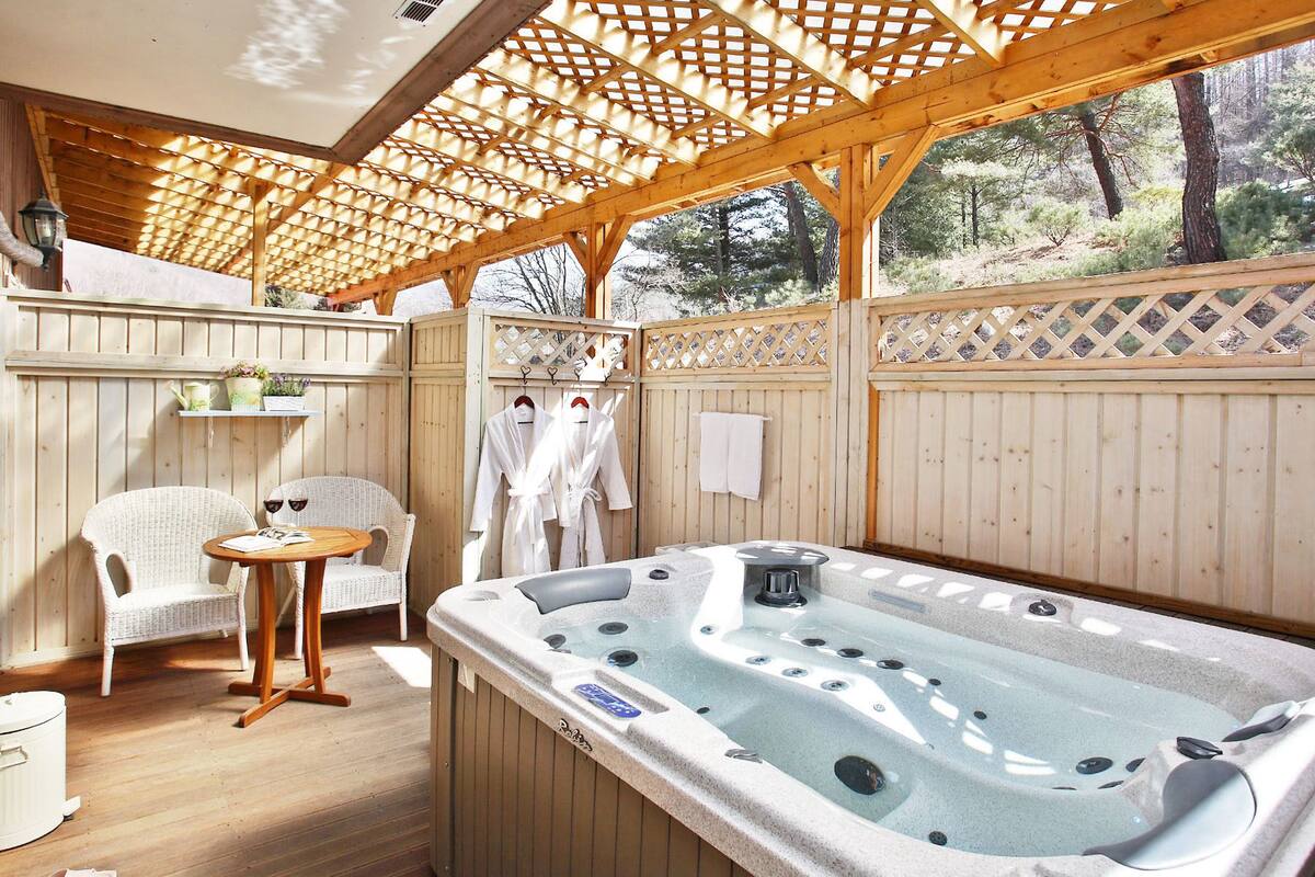 A wooden deck with a hot tub, wicker chairs, and a small table with a book and wine glasses.