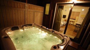 A hot tub in a room with wooden walls and a visible bathroom in the background. - Byeolmuri Pension (Hoengseong)