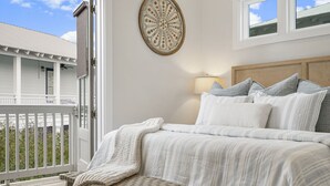 Une chambre à coucher avec un lit, des oreillers, une table de chevet, un élément de décoration murale et une vue sur un balcon et un immeuble.