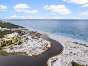 An aerial view of a coastal area with a beach, a river, and a building complex.