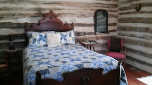 A log cabin room with a wooden bed, a red chair, a small table, and a mirror on the wall. - Butler Cabin at The Homestead B&B  (Dripping Springs,)