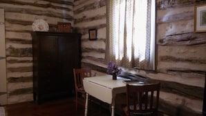 A log cabin interior with a wooden table, two chairs, a cabinet, and a window with curtains. - Butler Cabin at The Homestead B&B  (Dripping Springs,)