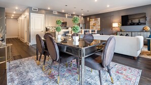 A modern kitchen with built-in appliances, a dining area with a glass table and velvet chairs, and a living area with a sofa and TV. - ⚜️Stylish,Spacious & Comfortable Downtown Penthouse! Enjoy The View from Your Personal Terrace! (New Orleans)