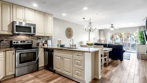 A modern kitchen with stainless steel appliances, a central island, and a dining area with a view of the outdoors.
