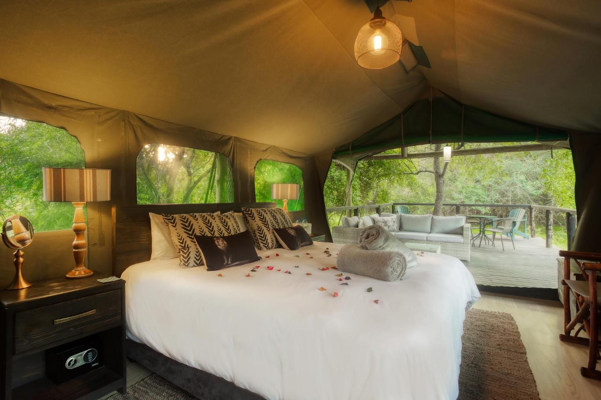 A tented accommodation room with a bed, bedside lamps, a mirror, and a view of the outdoors.