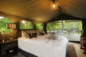 A tented accommodation room with a bed, bedside lamps, a mirror, and a view of the outdoors. - Camp Bethel (Hoedspruit)