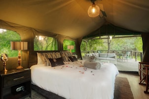 A tented accommodation room with a bed, bedside lamps, a mirror, and a view of the outdoors.