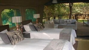 Ein Zimmer mit zwei Betten, jeweils mit weißer Bettwäsche und grauen Kissen, und einem hölzernen Kopfteil. Auf jedem Bett stehen zwei Lampen.
