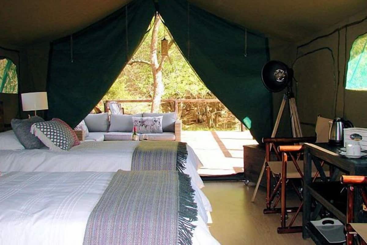 Alojamiento en carpa con cama, zona de estar y mesa con lámpara y hervidor.