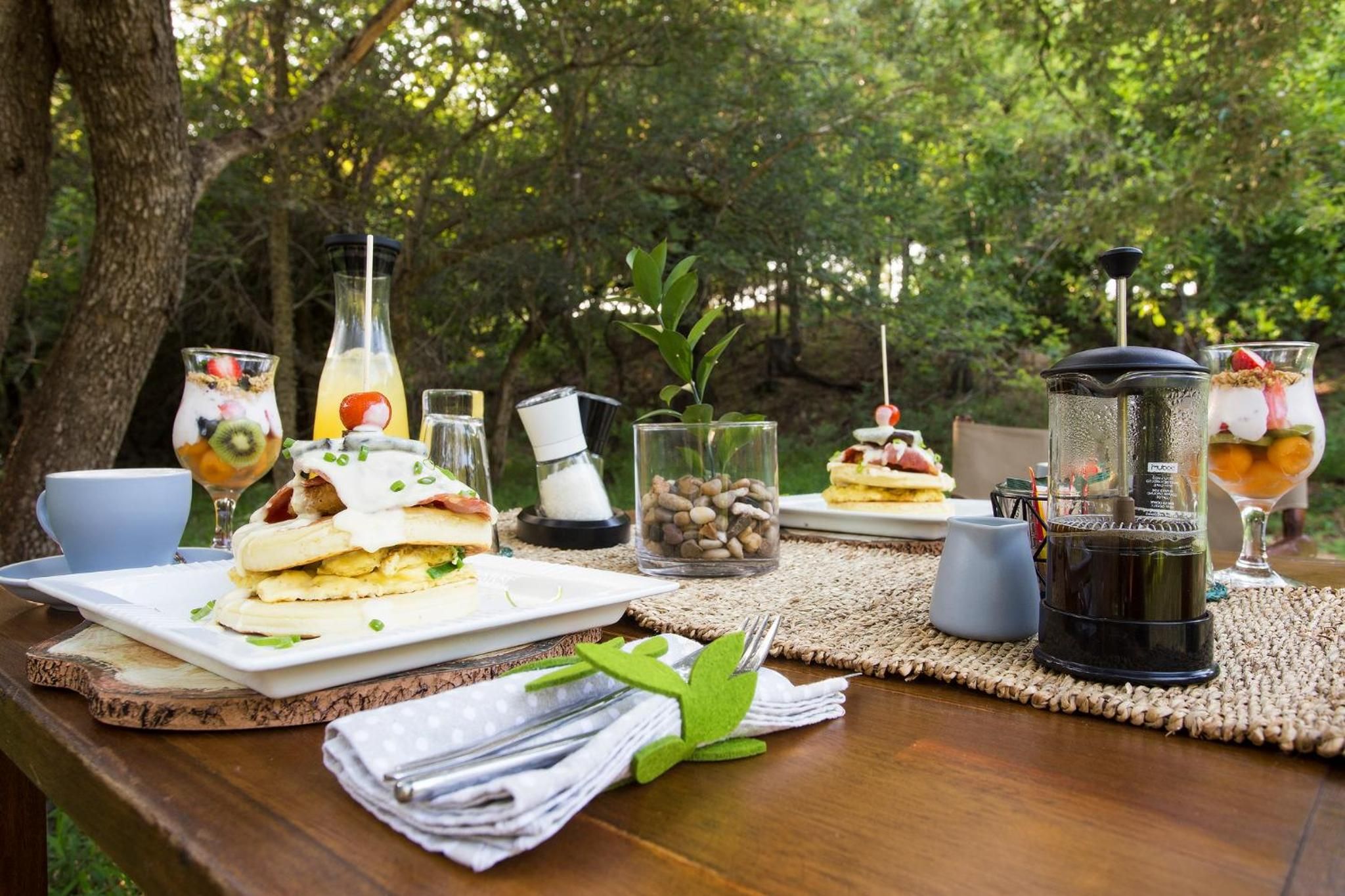 Mobiliario exterior para comer con sándwiches, bebidas y una cafetera sobre una mesa de madera.