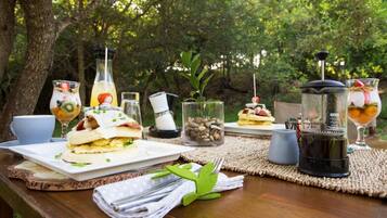 Mobiliario exterior para comer con sándwiches, bebidas y una cafetera sobre una mesa de madera.