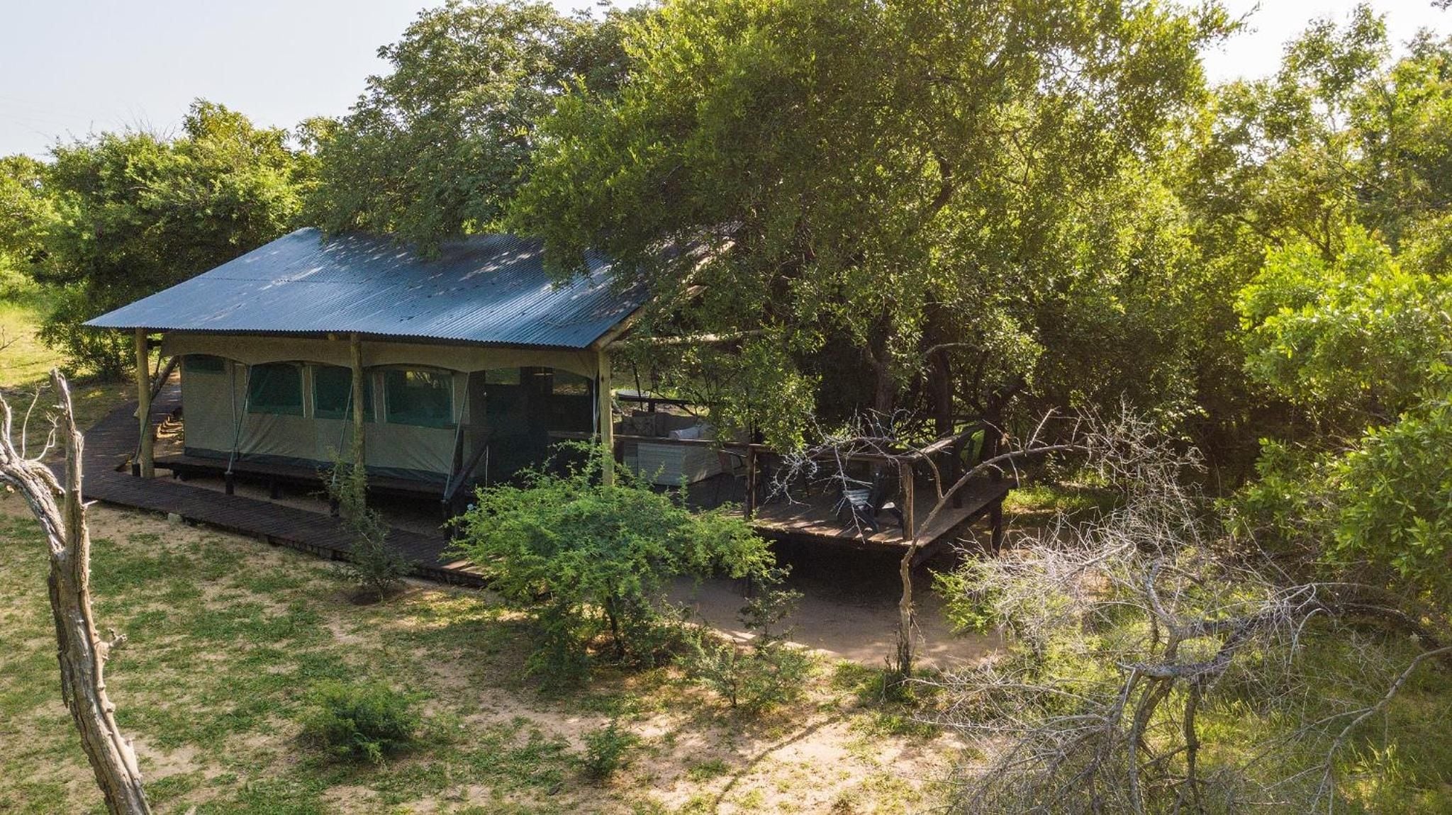 A small, single-story structure with a corrugated metal roof, surrounded by dense greenery and trees.