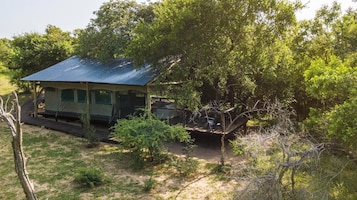 A small, single-story structure with a corrugated metal roof, surrounded by dense greenery and trees.