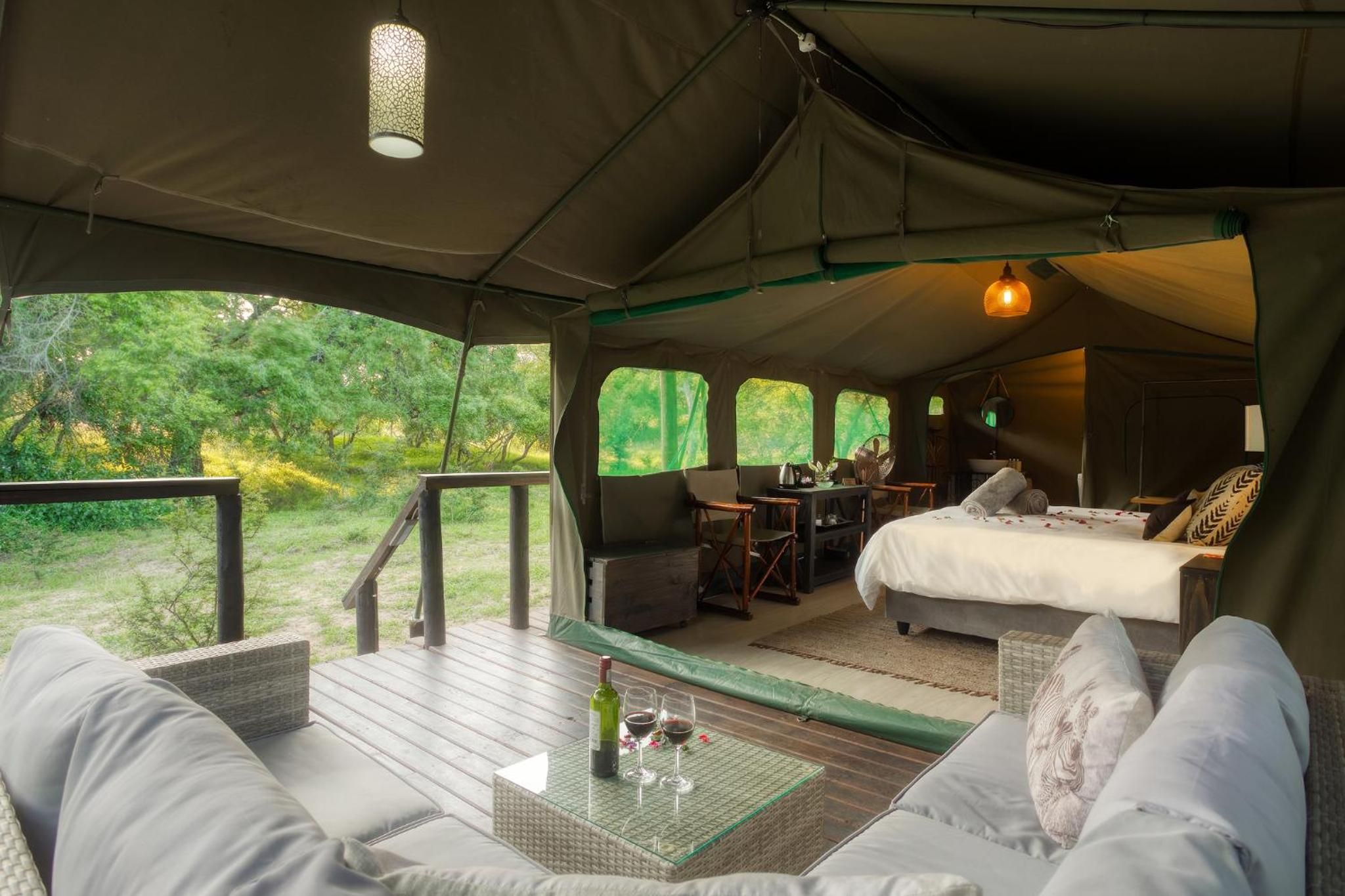 Een tentaccomodatie met een bed, zithoek en een tafel met een fles en glazen.