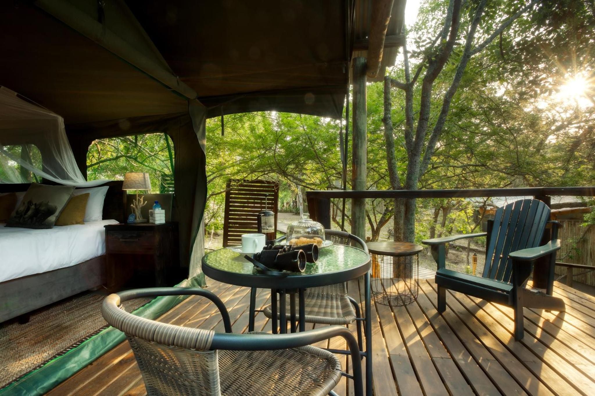 Un espace extérieur abrité comprenant un lit, une table, des chaises et une vue sur les arbres.