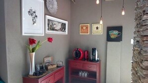 Ein Zimmer mit einer Kaffeestation, gerahmten Kunstwerken und einer Vase mit roten Blumen.