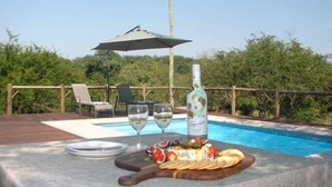 Ein Tisch am Pool mit einer Flasche, Gläsern und einer Obstplatte.