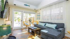 A living room with a grey sofa, two yellow wicker chairs, a wooden coffee table, and a TV mounted on the wall. - 3BR Captiva Cottage with Hot Tub & Steps to the Beach (Captiva)