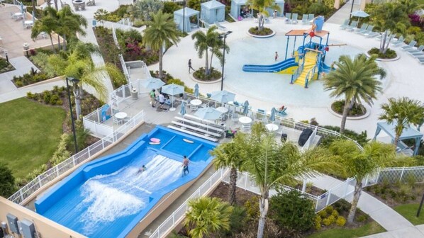 Vista aérea de un resort con una piscina grande, un tobogán de agua y una zona de juegos para niños.