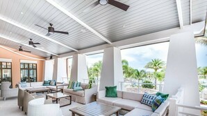 An outdoor lounge area with multiple seating options, ceiling fans, and large windows offering views of palm trees. - Colorful & Unique Private Pool 1561 (Kissimmee)