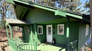 Una cabaña de madera verde con un porche, una puerta y una ventana.