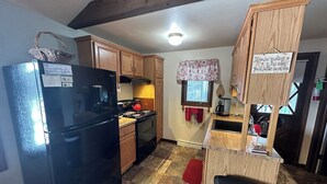 Una cocina compacta con un refrigerador negro, armarios de madera, una estufa y un lavamanos pequeño.