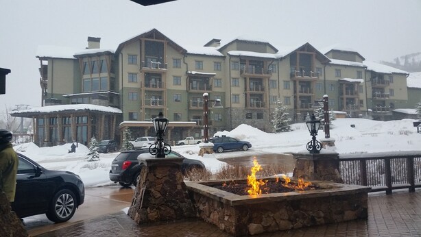 A snow-covered outdoor area with a stone fire pit and a building in the background.