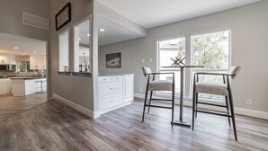 Een moderne keuken met witte kasten, een eethoek met twee stoelen, en een groot raam dat voor natuurlijk licht zorgt.