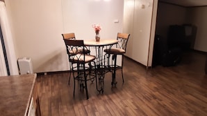 A dining area with a wooden table and four chairs, a vase with flowers, and a white wall.