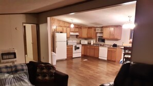 A living room with a sofa and a chair, a kitchen with wooden cabinets and white appliances, and a hallway leading to another room.