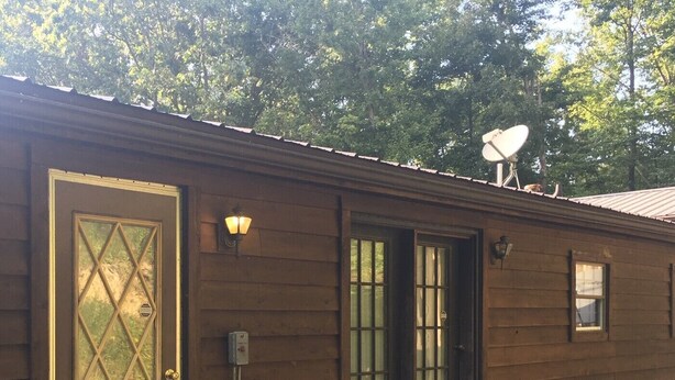 A wooden building with a large door, two windows, and a satellite dish on the roof.