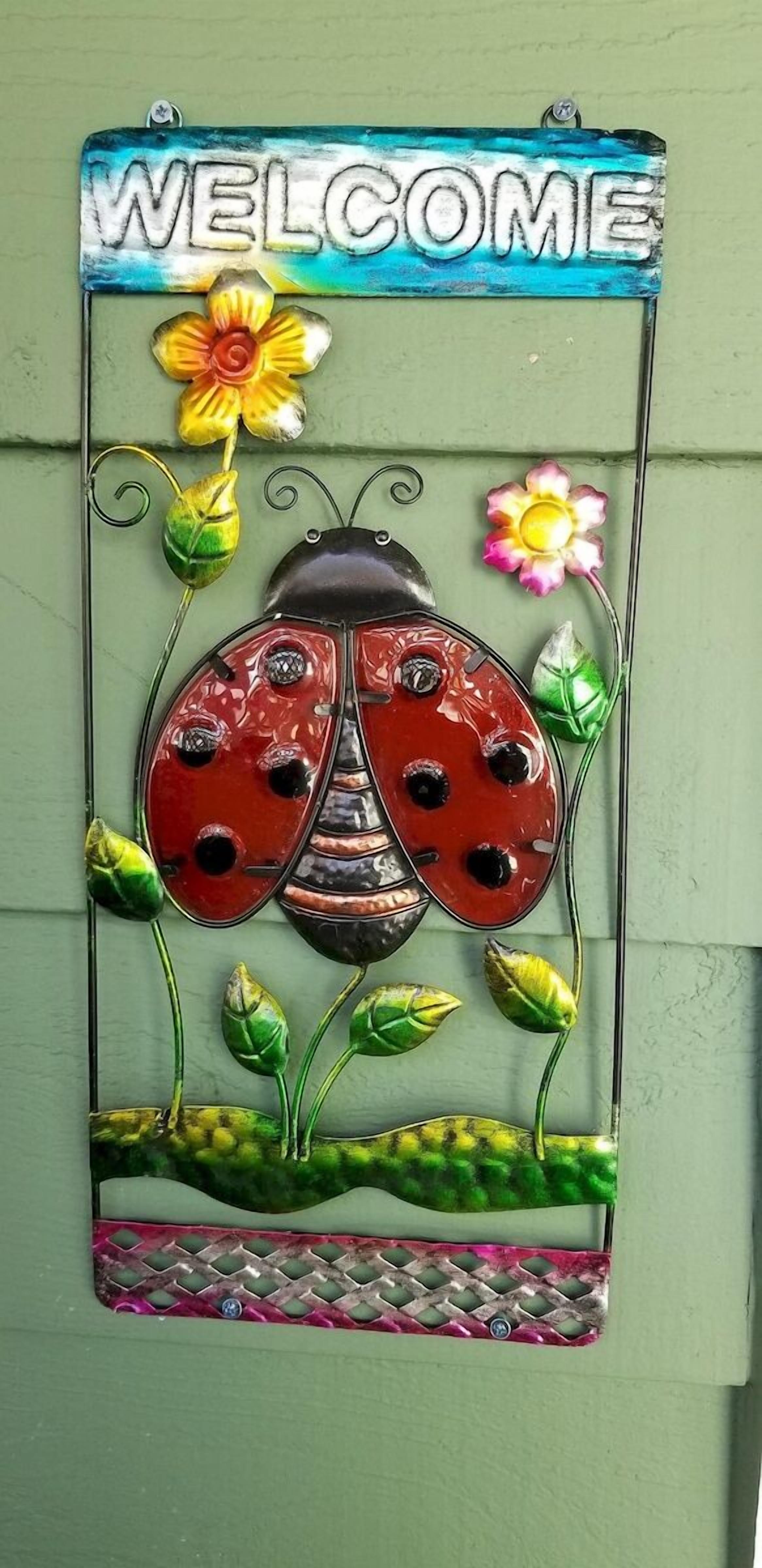 A decorative metal sign with a ladybug and flowers, mounted on a green wall.