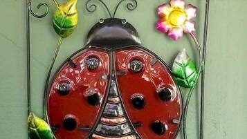 A decorative metal sign with a ladybug and flowers, mounted on a green wall.