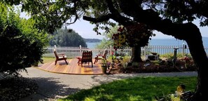 A wooden deck with outdoor seating, a white picket fence, and a view of a lake and hills.