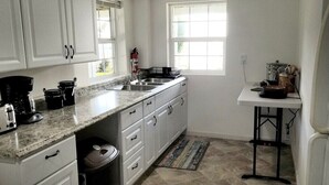 Una cocina con armarios blancos, encimera de granito, un lavabo, cafetera y ventana.