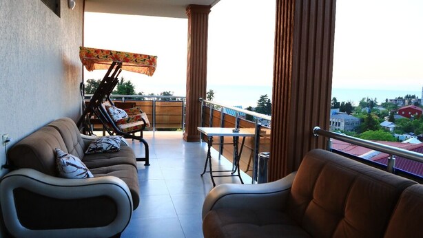 A balcony with a sofa, a table, and a chair, overlooking a coastal view. - Tamara bed and breakfast :-) (Batumi)