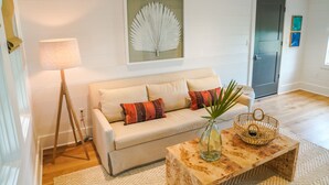 A living room with a sofa, a lamp, a framed artwork, and a coffee table with a vase and a basket. - Home Away from Home! Beautiful Carriage House in Seagrove Close to the Beach (Santa Rosa Beach)