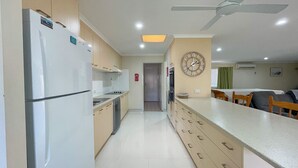 A modern kitchen with a refrigerator, stove, and microwave. There is a dining area with a table and chairs. - Sandy Paws - Burrum Heads- Walk to Beach -3BR- Aircon-Pool table (Burrum Heads)