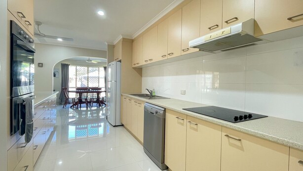A modern kitchen with a dishwasher, stove, and a dining area with a table and chairs. - Sandy Paws - Burrum Heads- Walk to Beach -3BR- Aircon-Pool table (Burrum Heads)