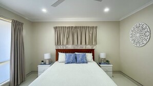 A bedroom with a large bed, two bedside tables with lamps, a headboard with curtains, and a decorative wall piece. - Sandy Paws - Burrum Heads- Walk to Beach -3BR- Aircon-Pool table (Burrum Heads)