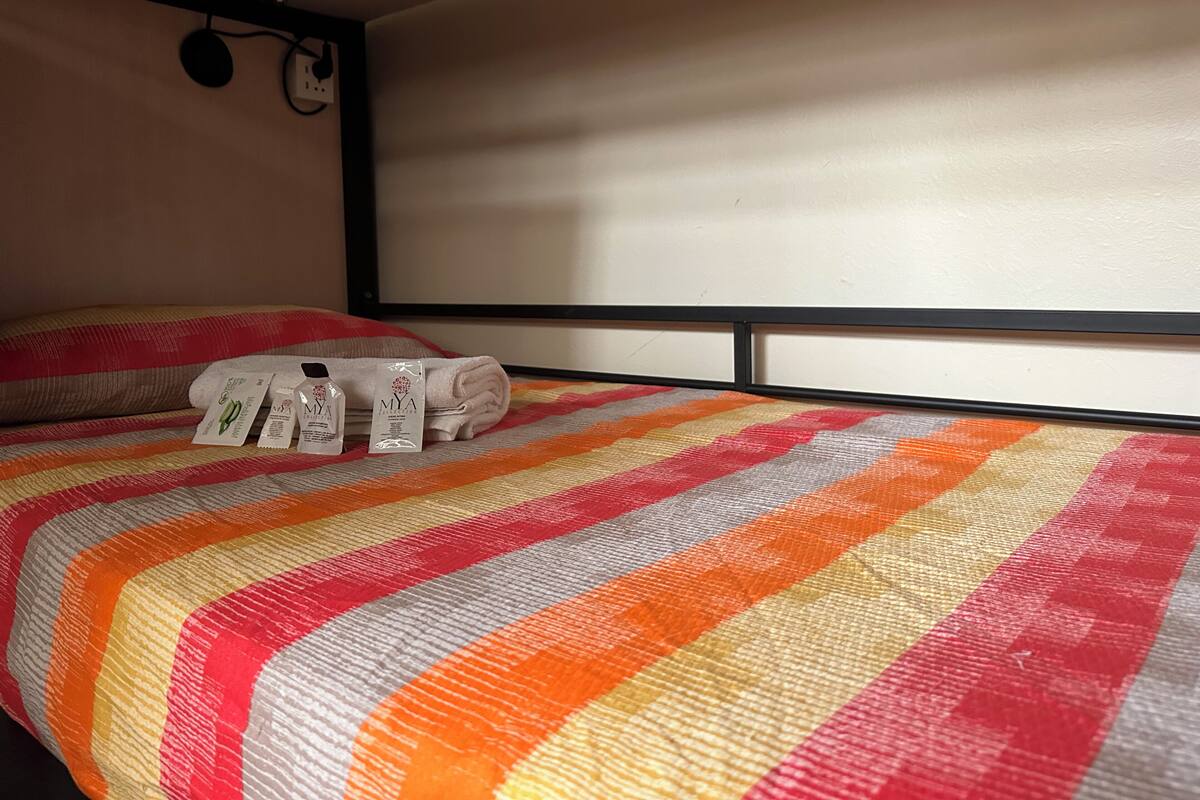 Una cama con un edredón a rayas, una toalla enrollada y un juego de artículos de aseo sobre la cama.