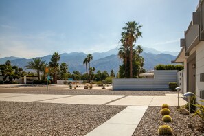 A modern building with a paved courtyard, palm trees, and a mountain backdrop.