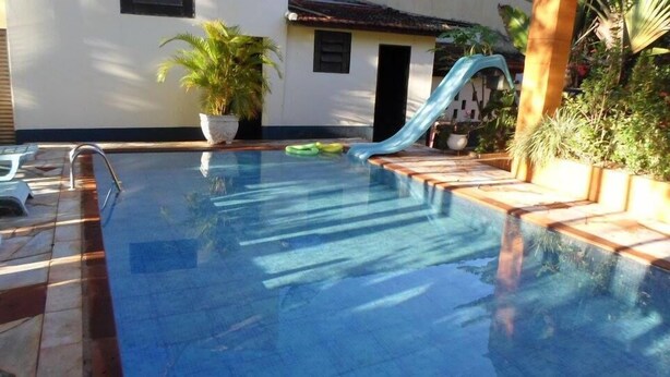 A clear blue swimming pool with a slide, surrounded by potted plants and a tiled deck.