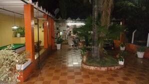 A covered outdoor area with a pool table, potted plants, and a tiled floor.